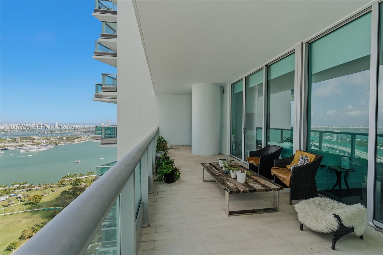 A high-rise balcony features a wooden coffee table, two wicker chairs, and a panoramic water view — 900 Biscayne Blvd # 4308, Miami FL 33132, MIAMI, FL