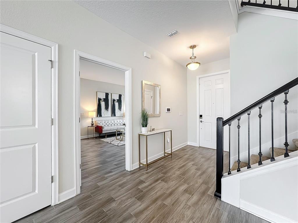 A foyer features wood-look tile flooring, a white front door, and a staircase with railings — 8886 FALLEN OAK DRIVE, DAVENPORT, FL