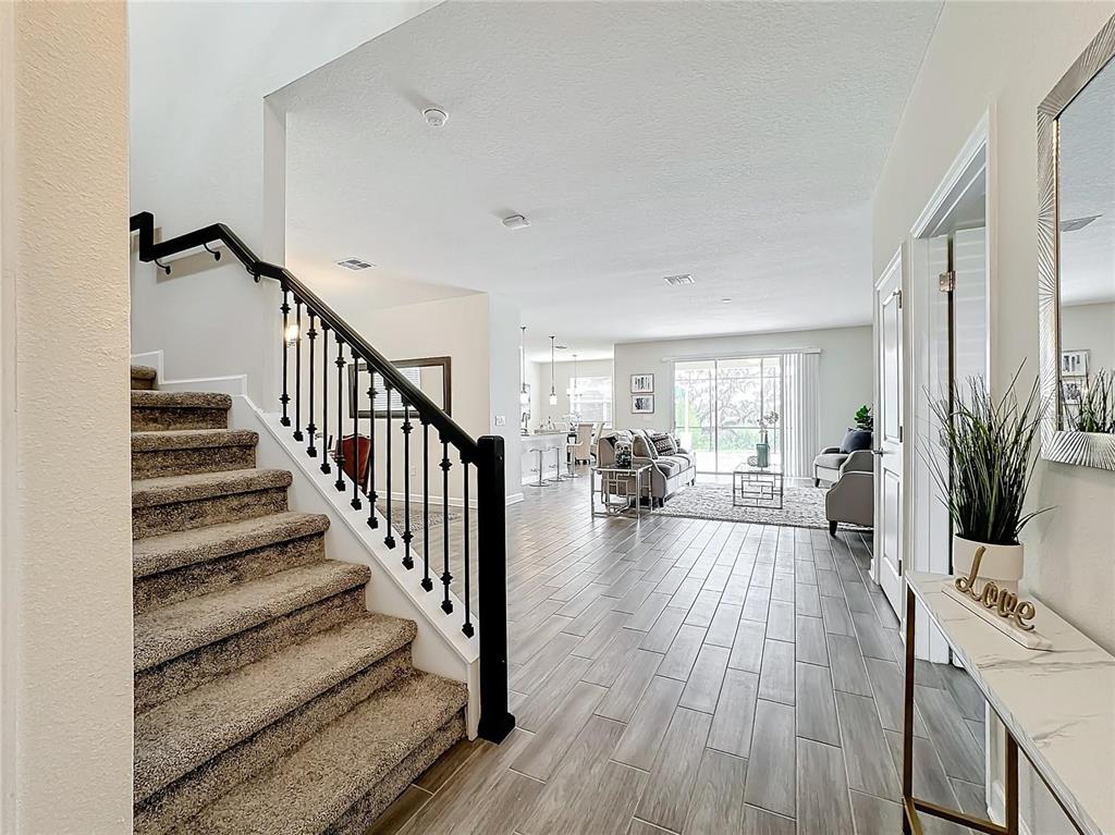 An entryway with carpeted stairs, wood-look tile flooring, and an open-concept living area beyond — 8886 FALLEN OAK DRIVE, DAVENPORT, FL