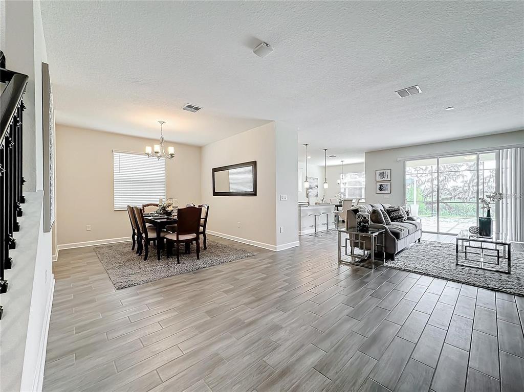 An open-concept living and dining area features wood-look tile flooring and a sliding glass door — 8886 FALLEN OAK DRIVE, DAVENPORT, FL