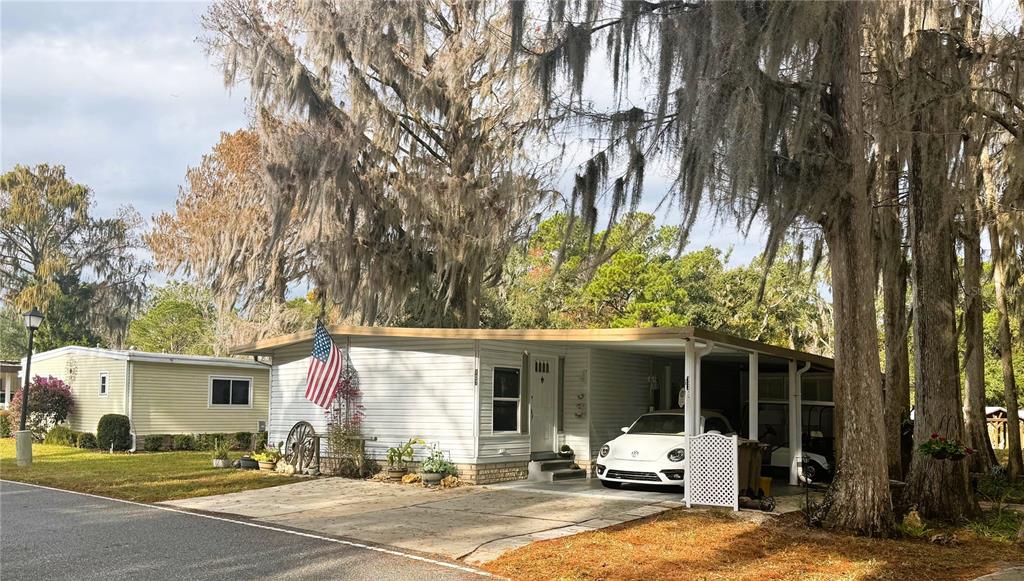 A white mobile home with a carport, a parked car, and large trees with Spanish moss — 107 ROYAL PALM DRIVE, LEESBURG, FL