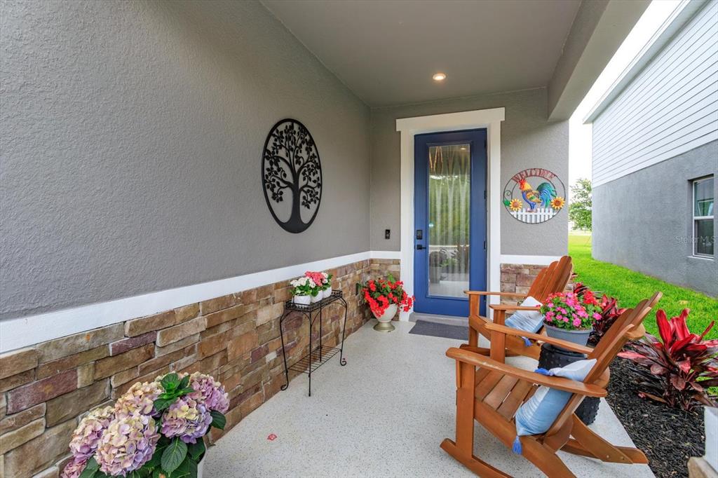 A covered front porch features a blue door, stone siding, and two wooden rocking chairs — 7016 LANIER FALLS ROAD, DELAND, FL