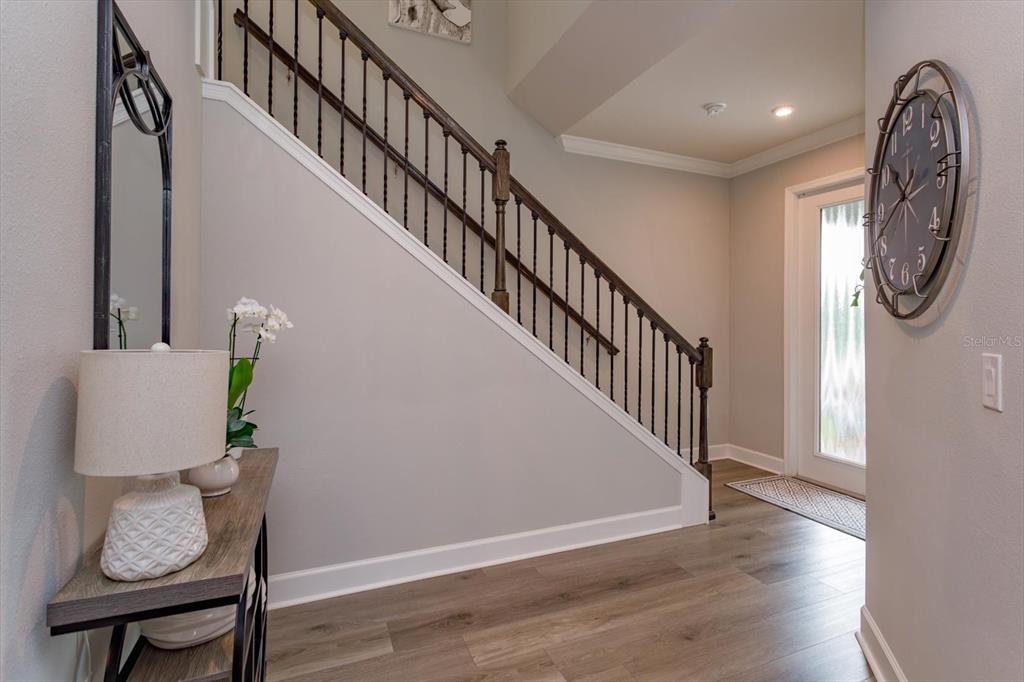 An entryway features a staircase with dark wood railings, wood-look flooring, and a wall clock — 7016 LANIER FALLS ROAD, DELAND, FL