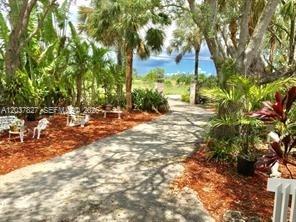 A paved driveway leads through a lush, tropical garden toward an open gate — HOMESTEAD, FL