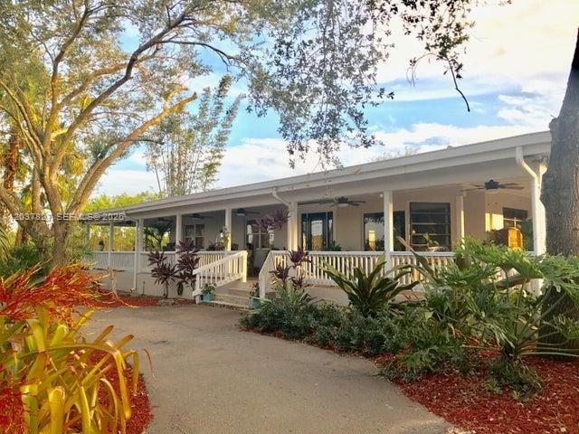 A single-story house with a wide covered porch and a paved driveway under large trees — HOMESTEAD, FL