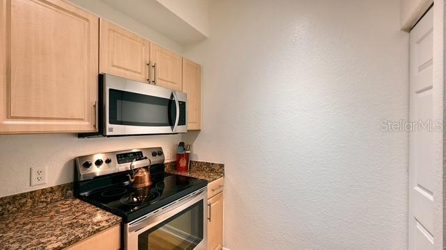 A kitchen featuring light wood cabinets, a stainless steel microwave, and a black electric range — 1064 N TAMIAMI TRAIL UNIT 1524, SARASOTA, FL