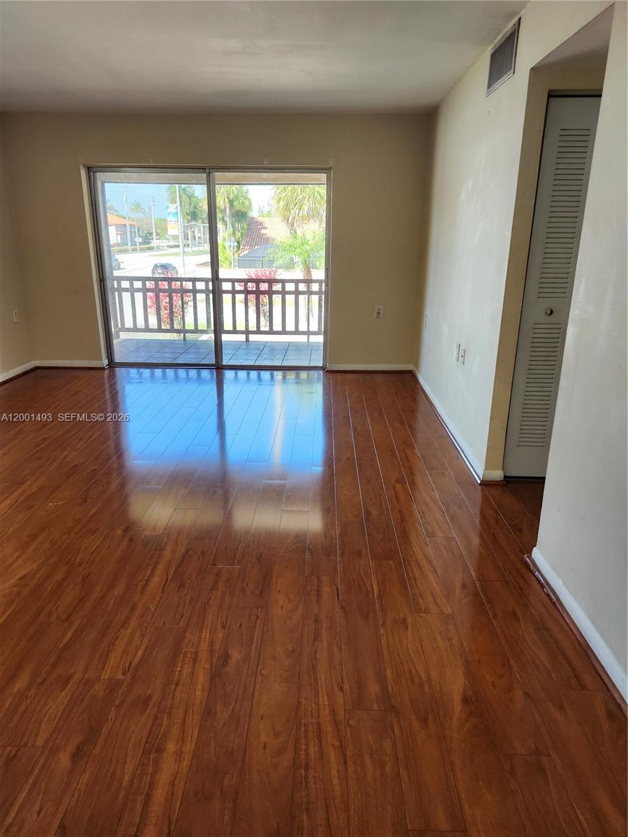 An empty room features polished hardwood flooring, beige walls, and a sliding glass balcony door — 11219 SW 88th St # 205C, Miami FL 33176, MIAMI, FL
