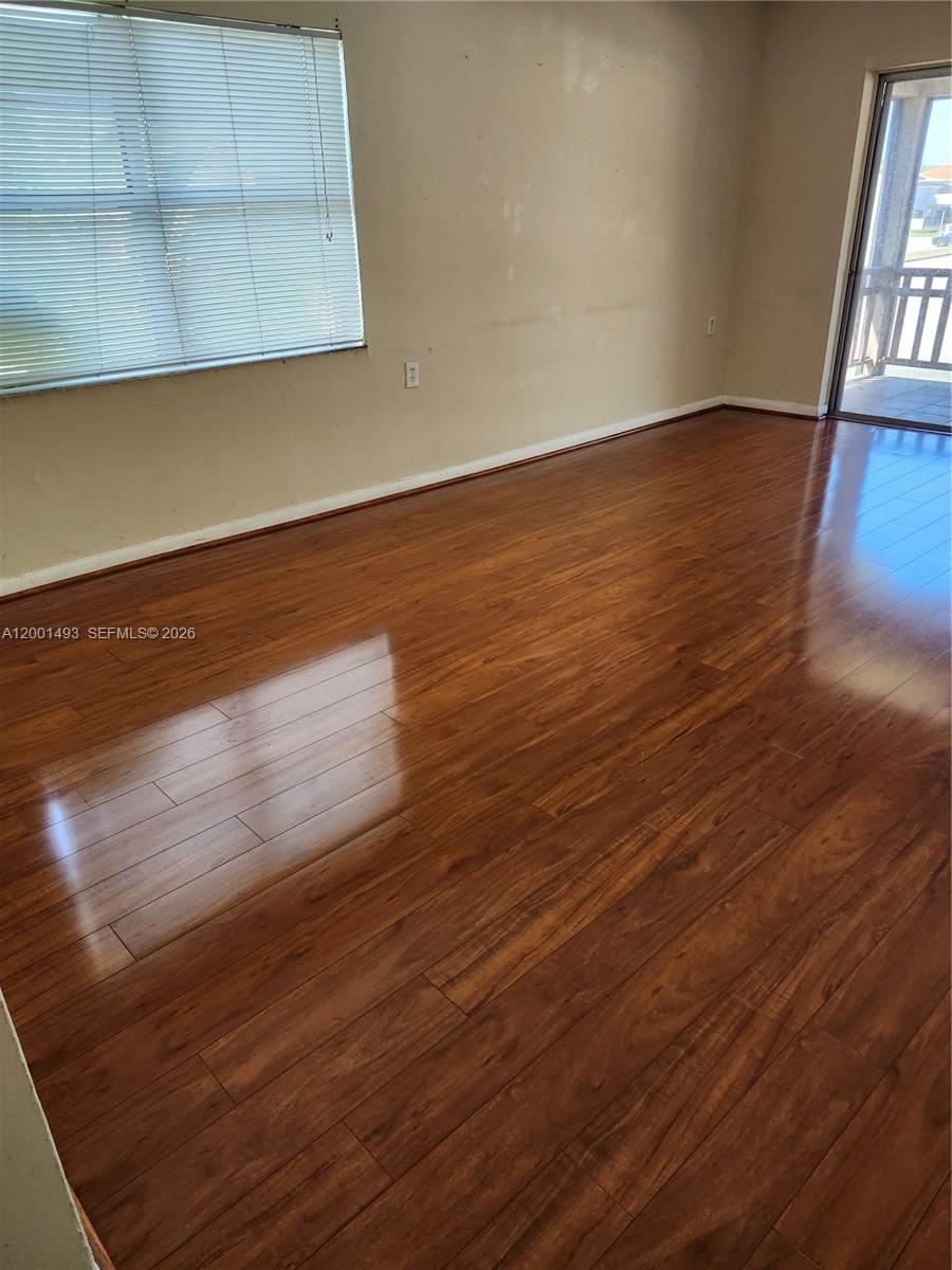 An empty room features wood-look laminate flooring, a window with blinds, and a sliding glass door — 11219 SW 88th St # 205C, Miami FL 33176, MIAMI, FL