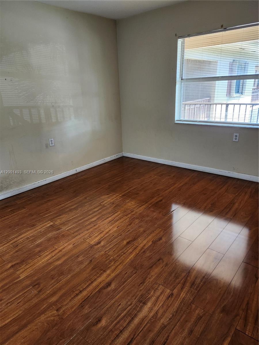 An empty room features wood-look laminate flooring, beige walls, and a window with blinds — 11219 SW 88th St # 205C, Miami FL 33176, MIAMI, FL