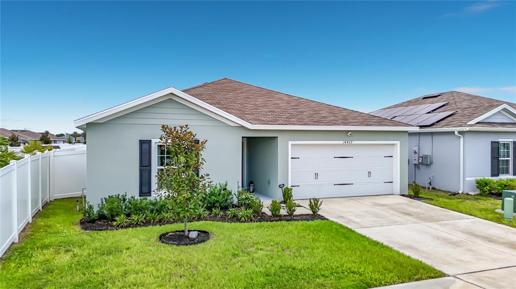 A light green single-story house with a two-car garage and a white vinyl fence — 14409 WHITEWATER WAY, BROOKSVILLE, FL