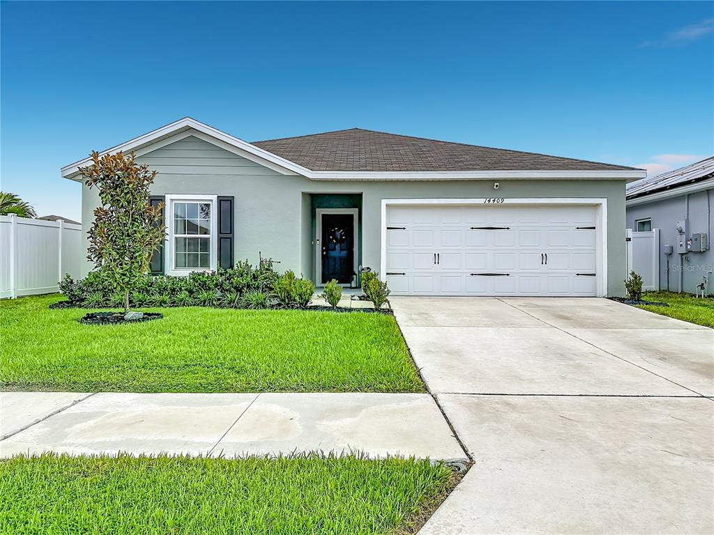 A single-story house with light green siding, a two-car garage, and a front lawn — 14409 WHITEWATER WAY, BROOKSVILLE, FL