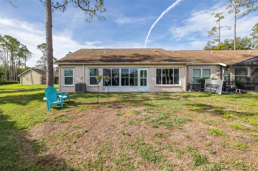 The exterior rear view of a single-story house features a screened porch and lawn — 9519 SCENIC PINE COURT, NEW PORT RICHEY, FL