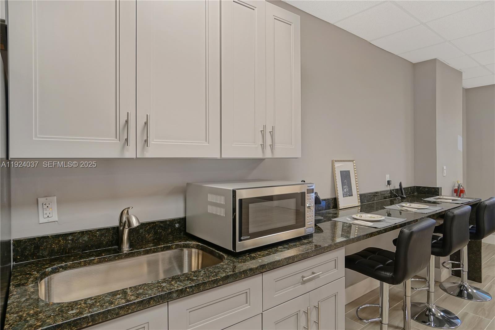 A kitchenette features light gray cabinets, a dark granite countertop, a sink, and bar seating — 12550 Biscayne Blvd # 902, North Miami FL 33181, NORTH MIAMI, FL