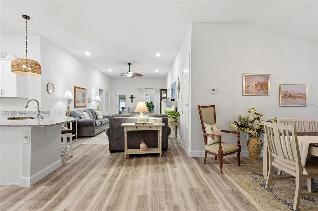 An open-concept living and dining area features light wood flooring, a kitchen island, and furniture — 203 SW SILVER PALM DRIVE, LAKE CITY, FL