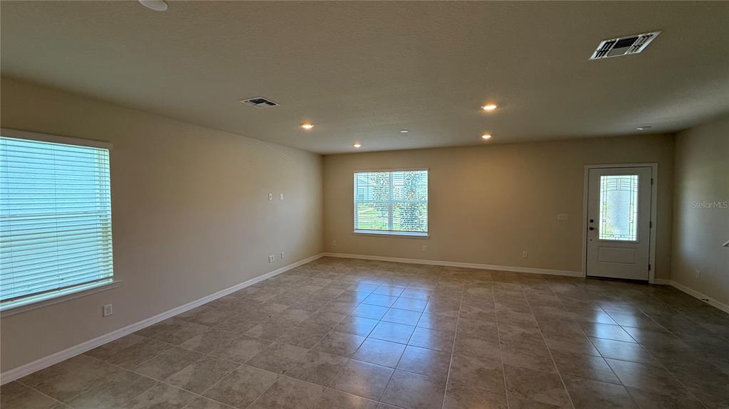 An empty living room features beige walls, tile flooring, recessed lighting, and two windows — 5025 FURROWED WAY, ST CLOUD, FL