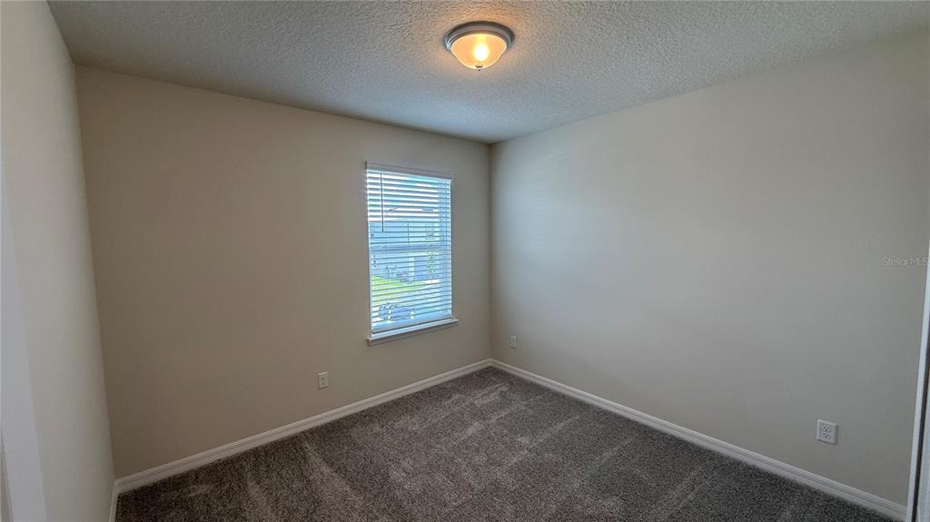 An empty bedroom features beige walls, gray carpet, a single window, and a ceiling light — 5025 FURROWED WAY, ST CLOUD, FL