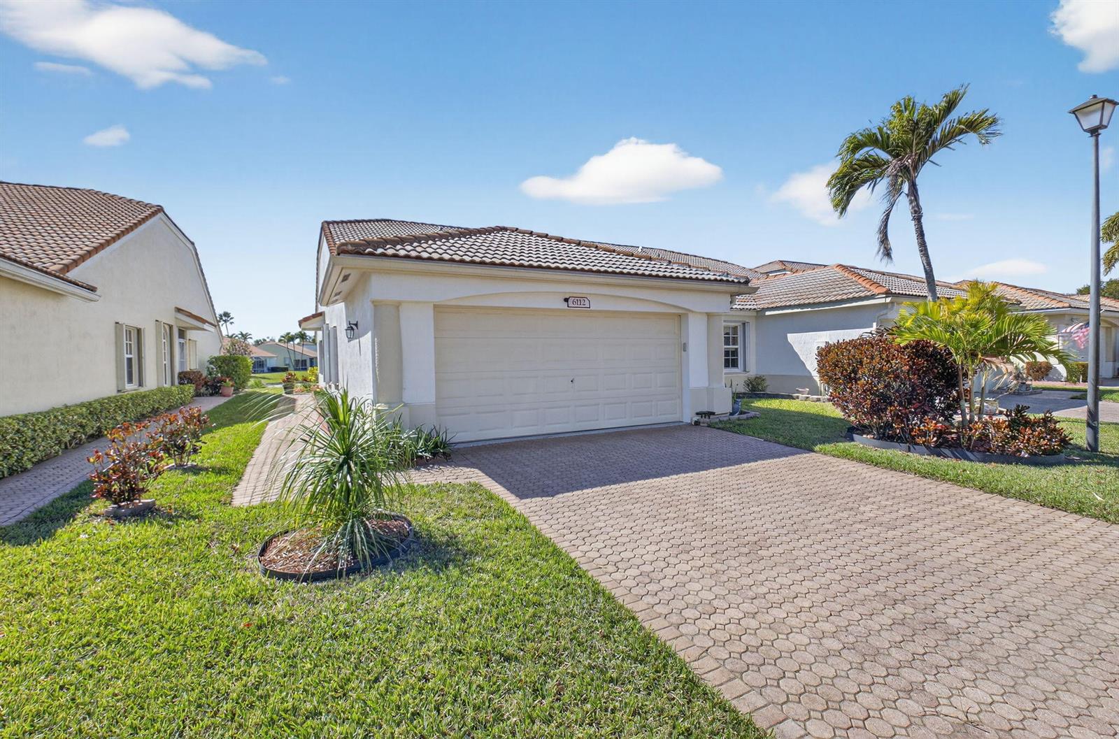 A single-story house with a beige stucco exterior, tiled roof, and a paved driveway — 6112 Caladium Road, Delray Beach FL 33484, DELRAY BEACH, FL