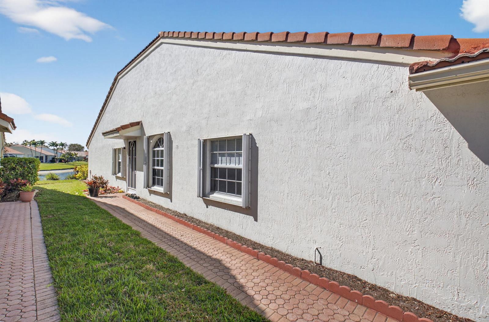 A side view of a stucco house with a tiled roof and a brick walkway — 6112 Caladium Road, Delray Beach FL 33484, DELRAY BEACH, FL