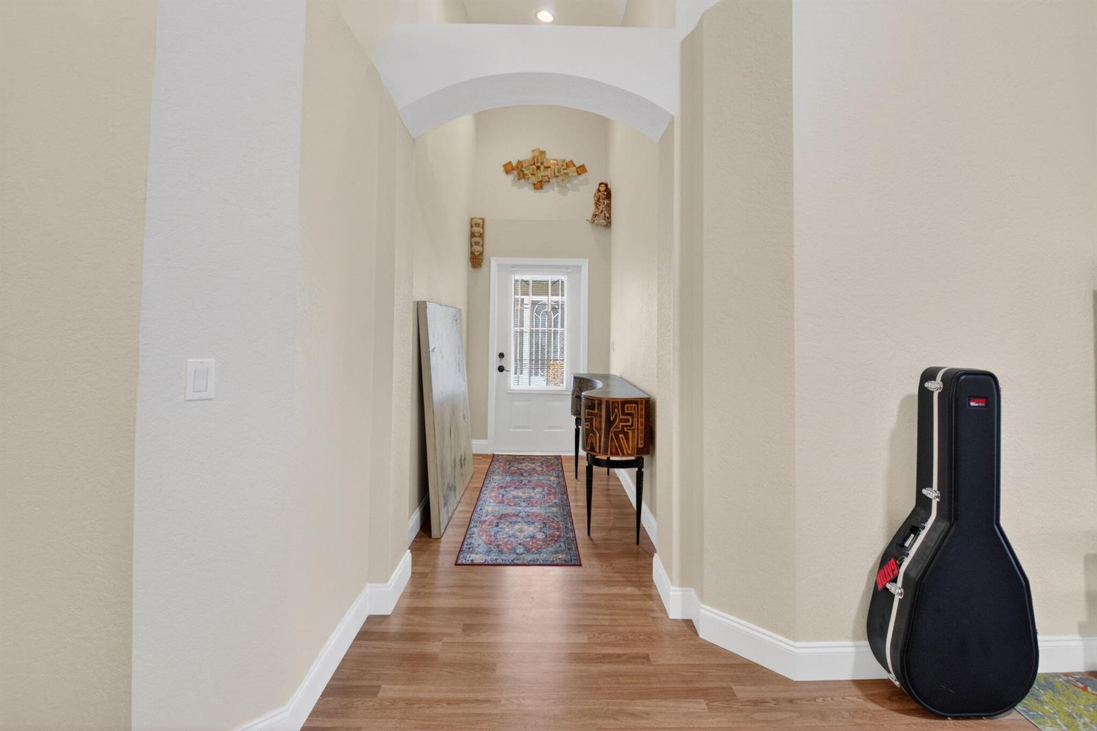 A hallway with wood-look flooring leads to a white front door under an arched ceiling — 6112 Caladium Road, Delray Beach FL 33484, DELRAY BEACH, FL