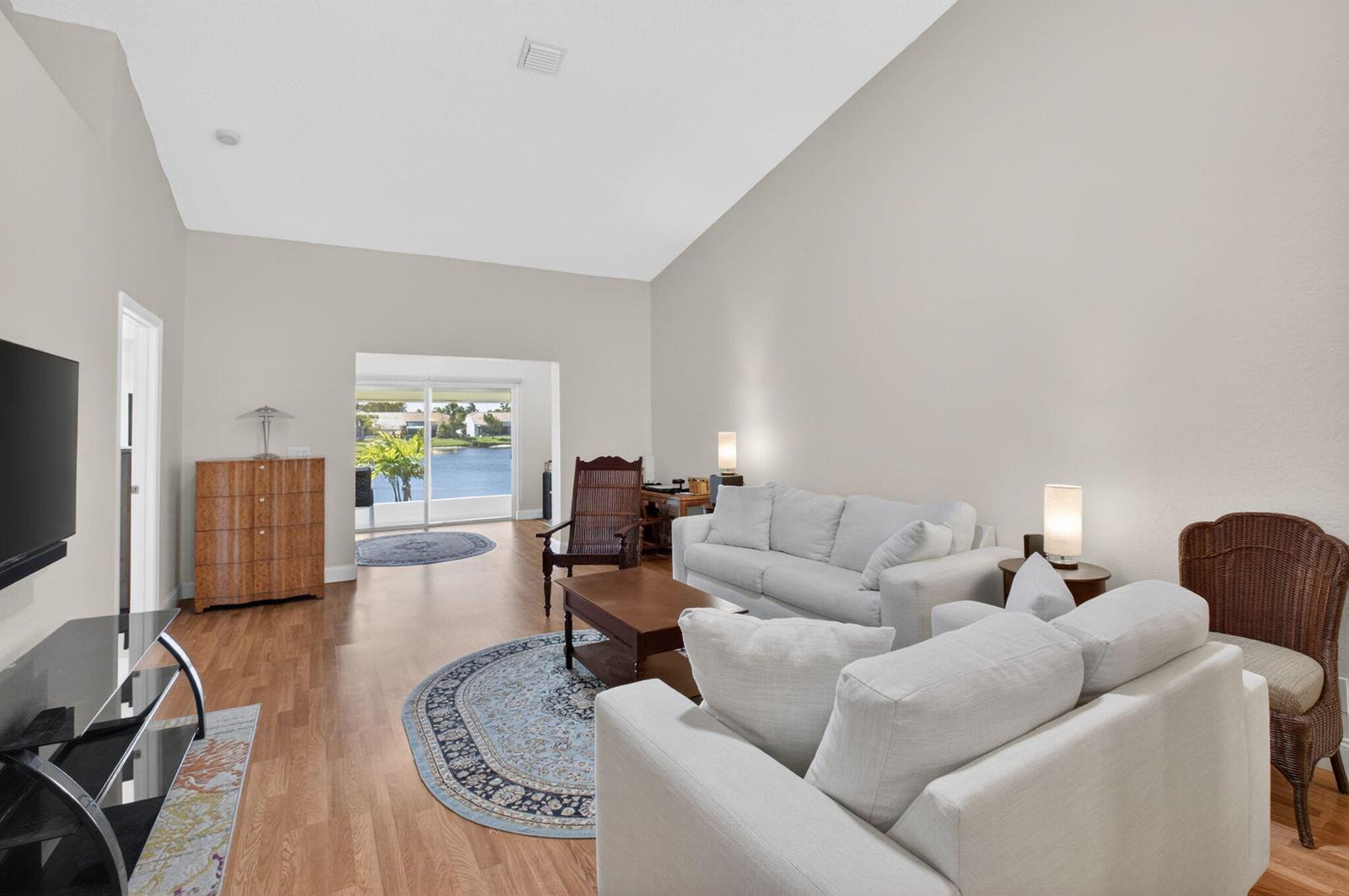 A living room with light-colored walls, wood flooring, two white sofas, and a lake view — 6112 Caladium Road, Delray Beach FL 33484, DELRAY BEACH, FL