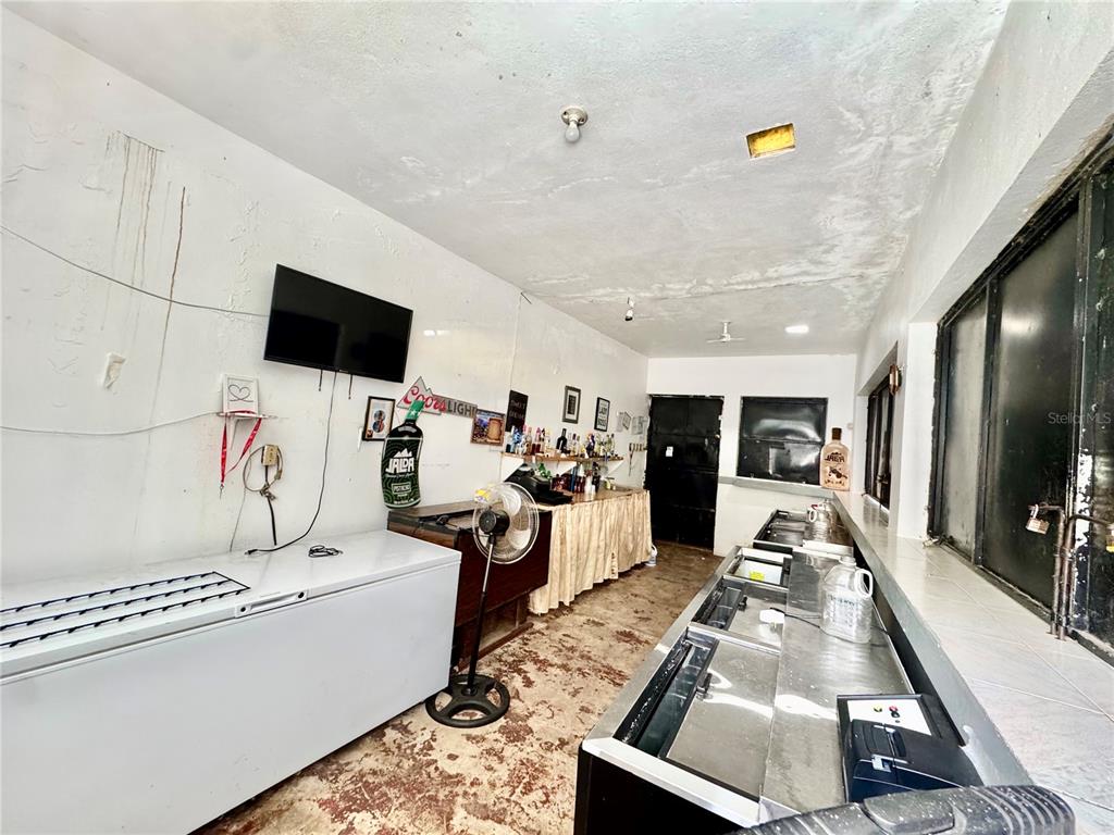 A commercial bar area features a chest freezer, stainless steel prep counters, and a pedestal fan — Barrio Quebrada Yeguas LA PLENA 94, SALINAS, PR