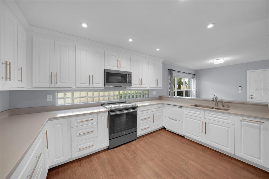A kitchen features white cabinets, stainless steel appliances, and wood-look flooring — 15876 SANCTUARY DRIVE, TAMPA, FL