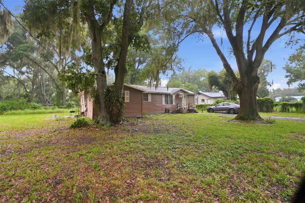 A single-story brown house with a metal roof sits on a grassy lot with trees — 5818 CHERRY ROAD, LAKELAND, FL