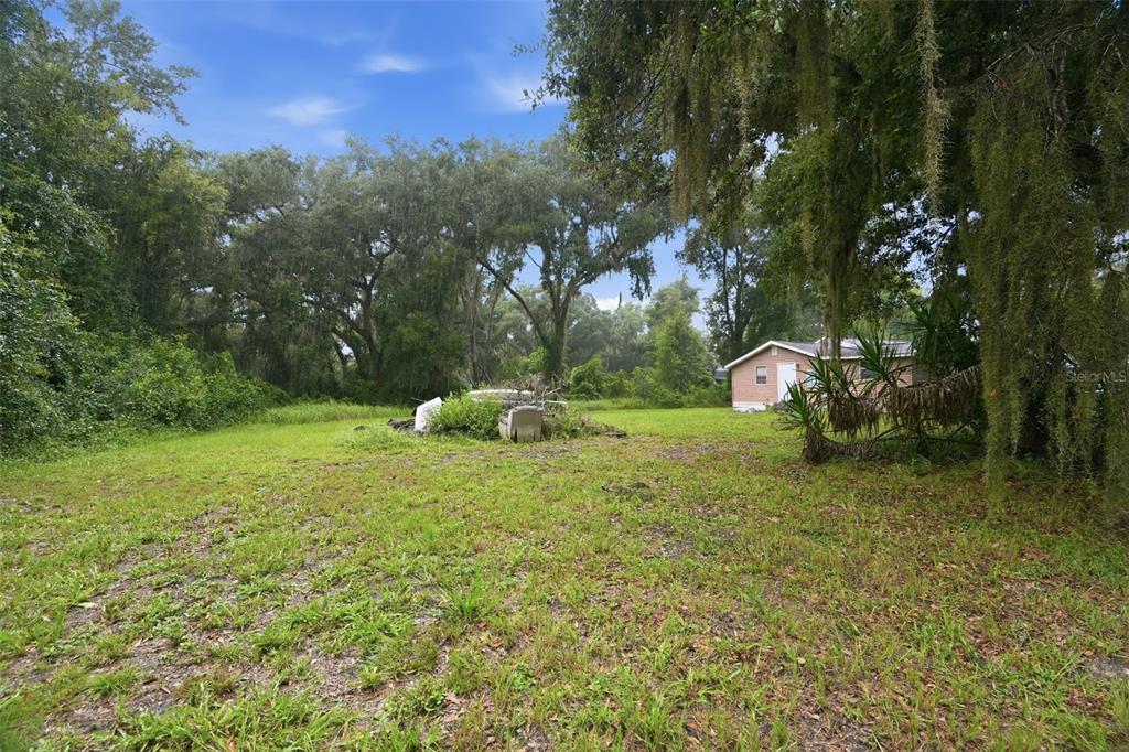 A grassy yard with scattered debris leads to a small house under large oak trees — 5818 CHERRY ROAD, LAKELAND, FL