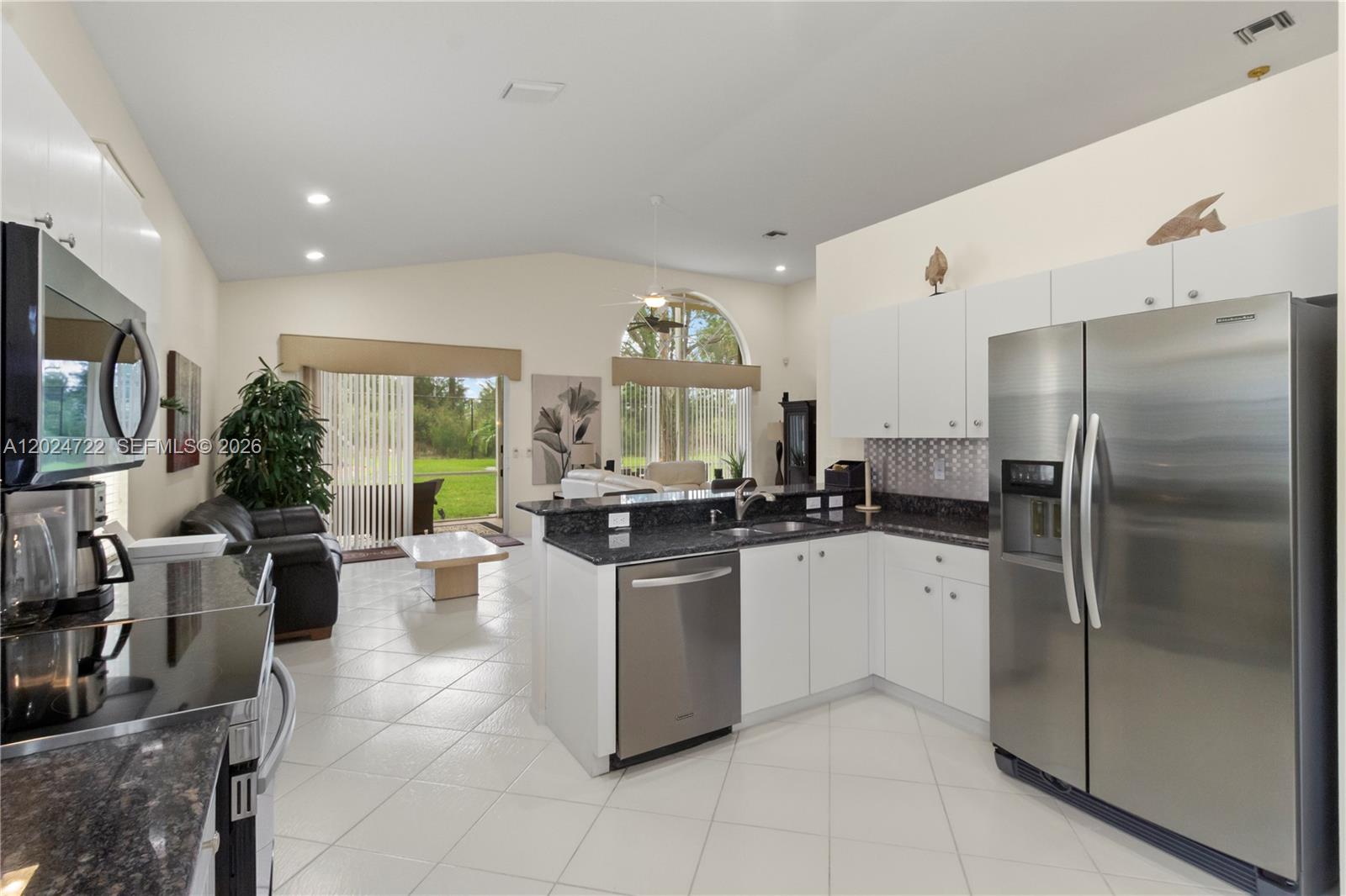 A kitchen with white cabinets and dark countertops overlooks a living area with tile floors — 10776 Grande Palladium Way, Boynton Beach FL 33436, BOYNTON BEACH, FL