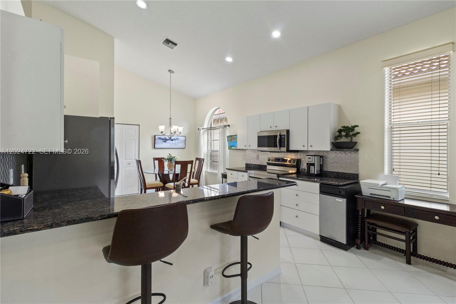 A kitchen features white cabinets, dark granite countertops, a breakfast bar, and an adjacent dining area — 10776 Grande Palladium Way, Boynton Beach FL 33436, BOYNTON BEACH, FL