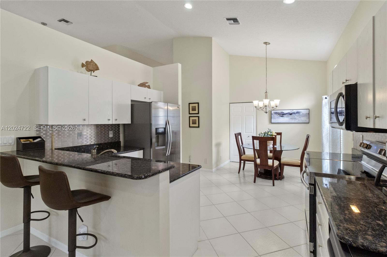 A kitchen with dark granite countertops and white cabinets opens to a dining area — 10776 Grande Palladium Way, Boynton Beach FL 33436, BOYNTON BEACH, FL