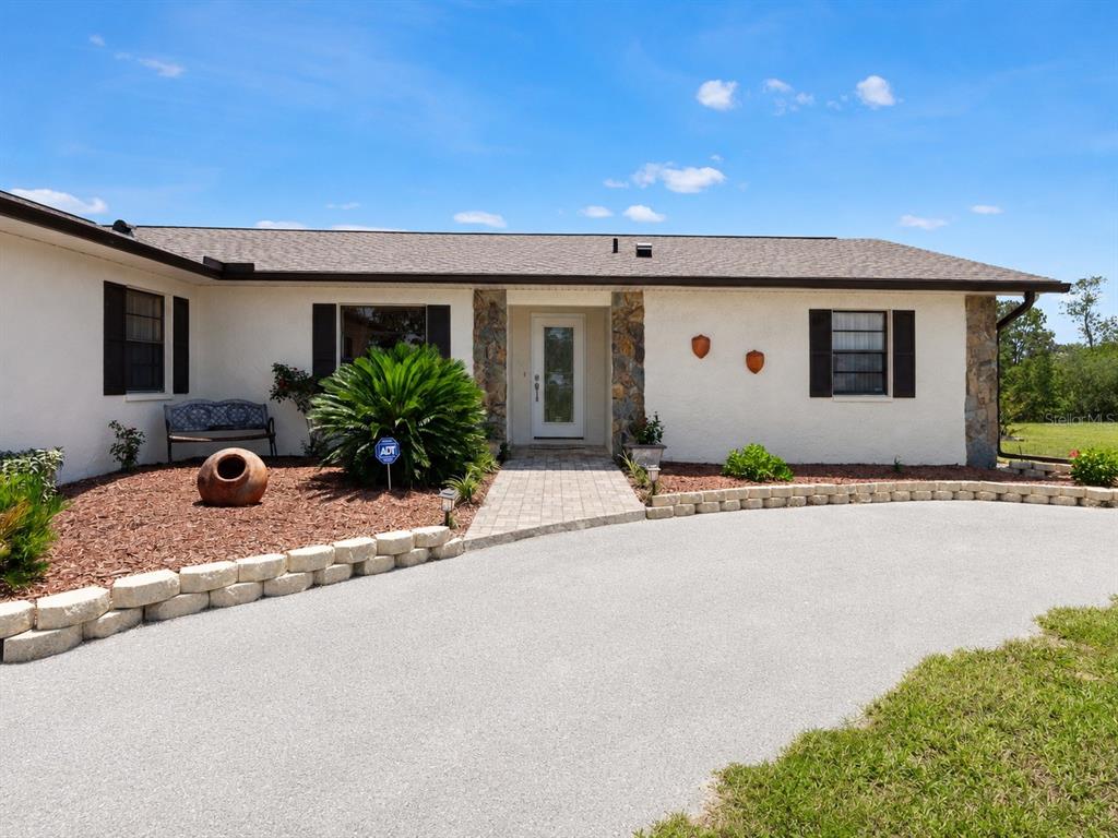 A single-story house with a white stucco facade, stone accents, and a paved driveway — 13260 TAYLOR STREET, BROOKSVILLE, FL