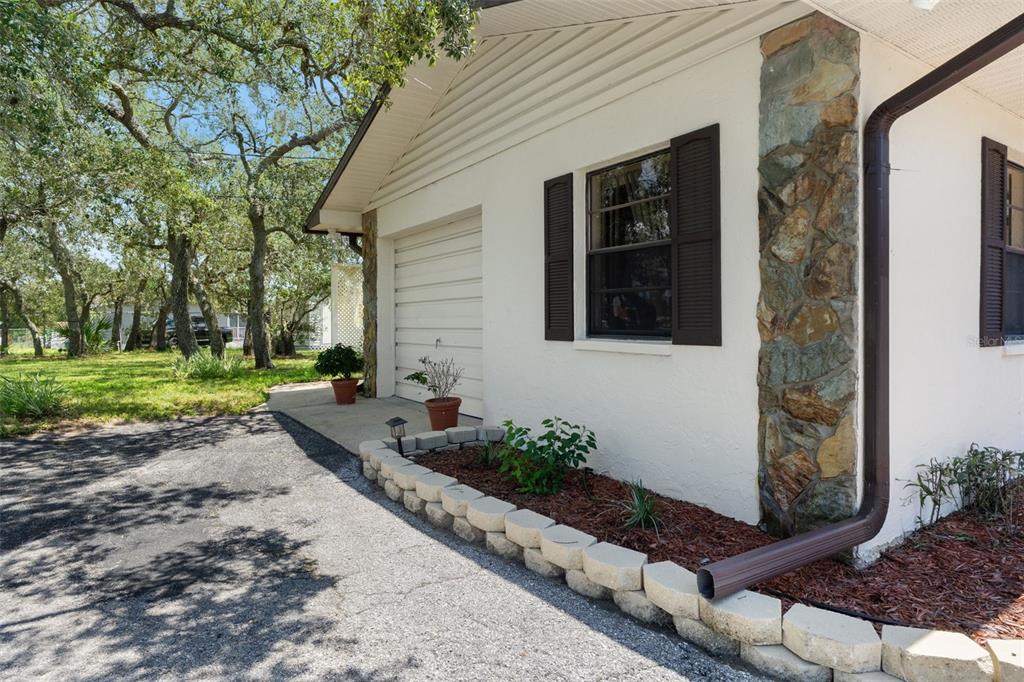 A white house exterior features a garage, a stone accent pillar, and a landscaped garden bed — 13260 TAYLOR STREET, BROOKSVILLE, FL