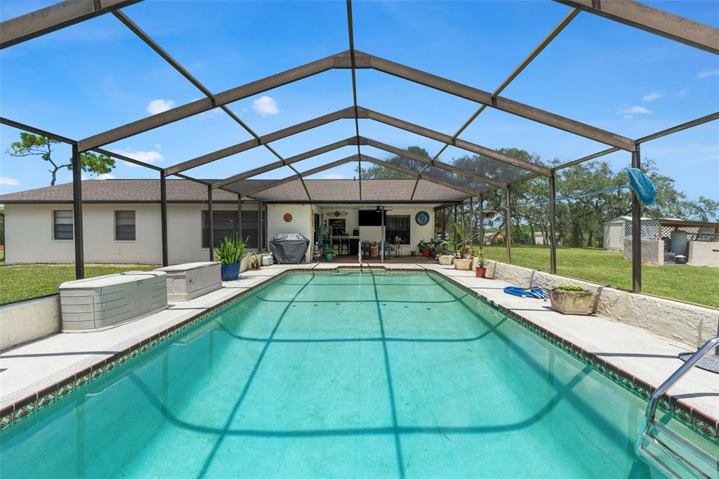 A rectangular swimming pool is enclosed by a screened lanai behind a single-story house — 13260 TAYLOR STREET, BROOKSVILLE, FL