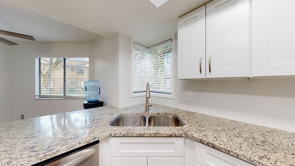A kitchen features white cabinets, granite countertops, a double-basin sink, and corner windows — 15 PINE HURST PLACE UNIT 15, PALM COAST, FL