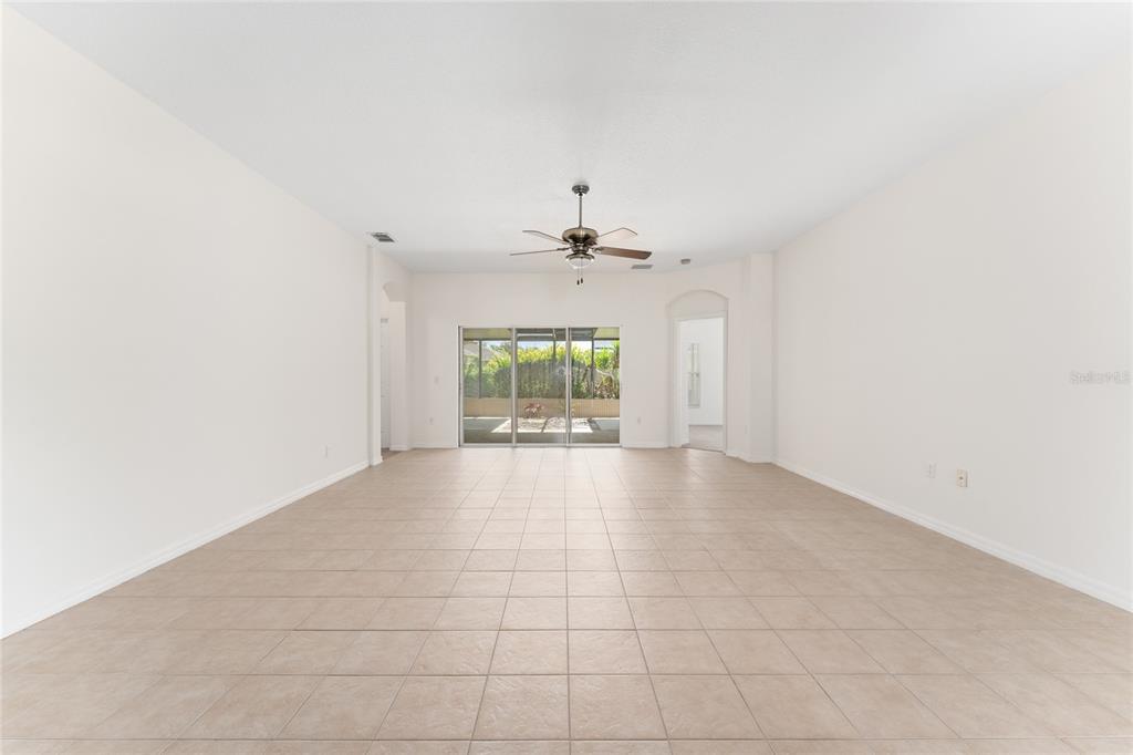 An empty living room with beige tile flooring, white walls, and sliding glass patio doors — 106 VISTA DRIVE, KISSIMMEE, FL