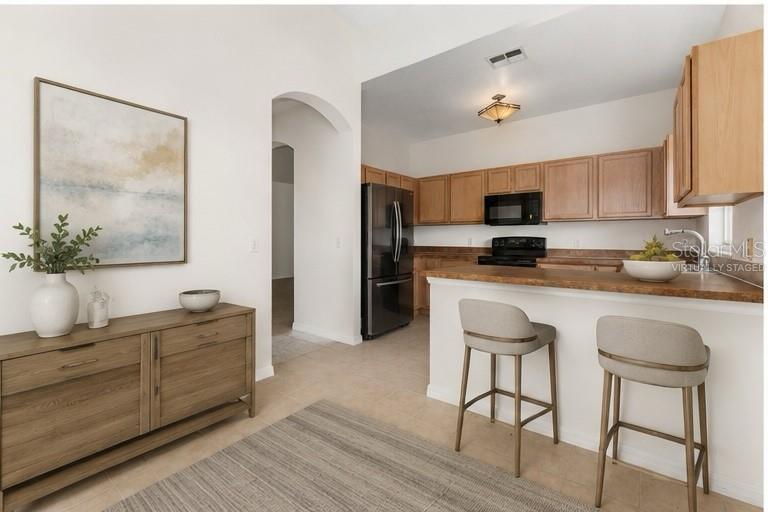 A kitchen with wood cabinets and a breakfast bar overlooks a dining area with furniture — 106 VISTA DRIVE, KISSIMMEE, FL