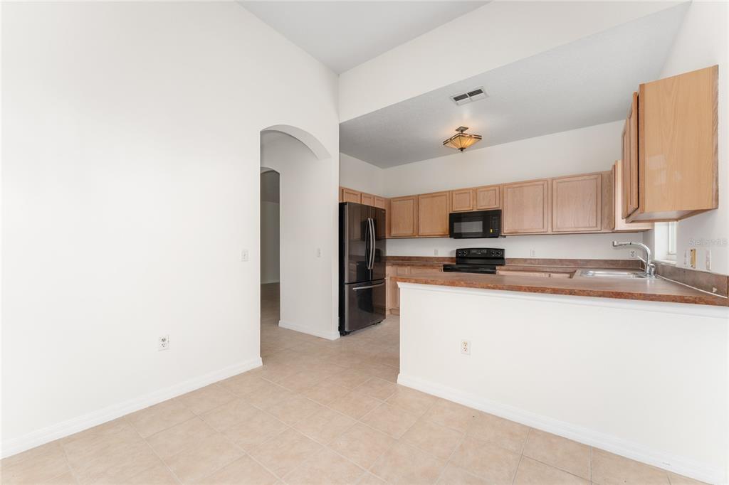 A kitchen with light wood cabinets, dark countertops, and black appliances overlooks a tiled area — 106 VISTA DRIVE, KISSIMMEE, FL