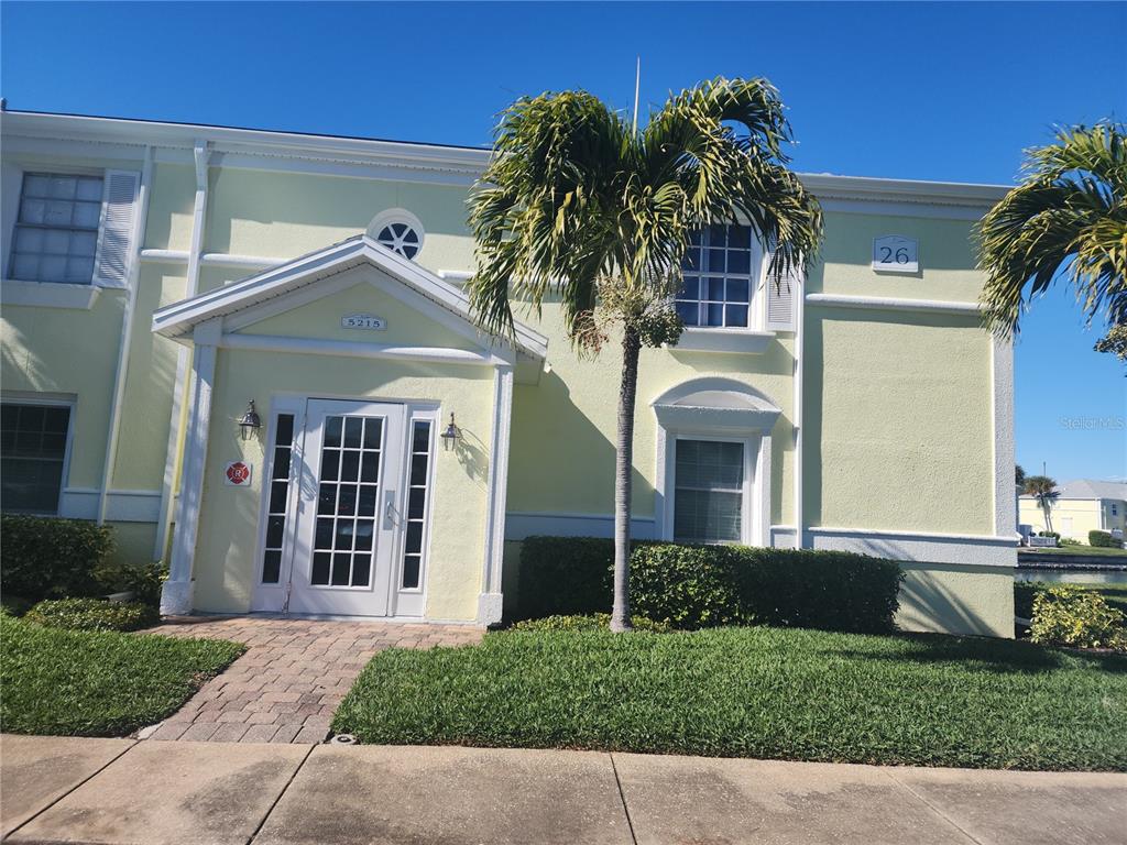 A two-story yellow building features a white-framed entrance, palm trees, and a paved walkway — 5215 COQUINA KEY DRIVE SE UNIT B, ST PETERSBURG, FL