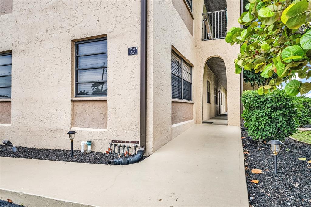 A beige stucco apartment building exterior features a covered walkway, dark-framed windows, and landscaping — 1217 AQUI ESTA DRIVE UNIT 5, PUNTA GORDA, FL