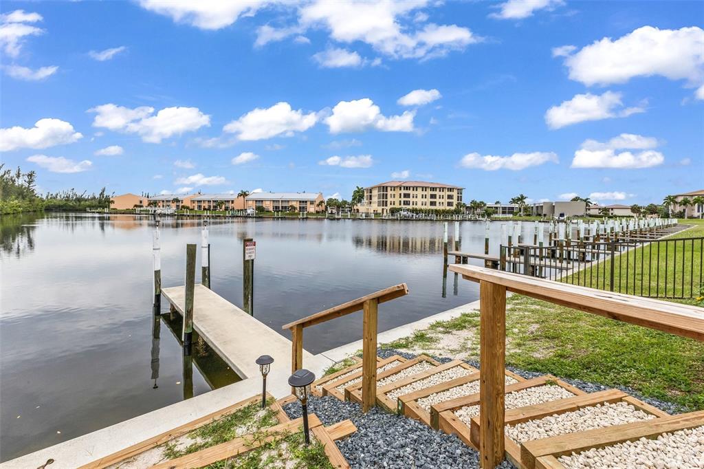 A wooden staircase leads down to a concrete boat dock on a calm canal — 1217 AQUI ESTA DRIVE UNIT 5, PUNTA GORDA, FL