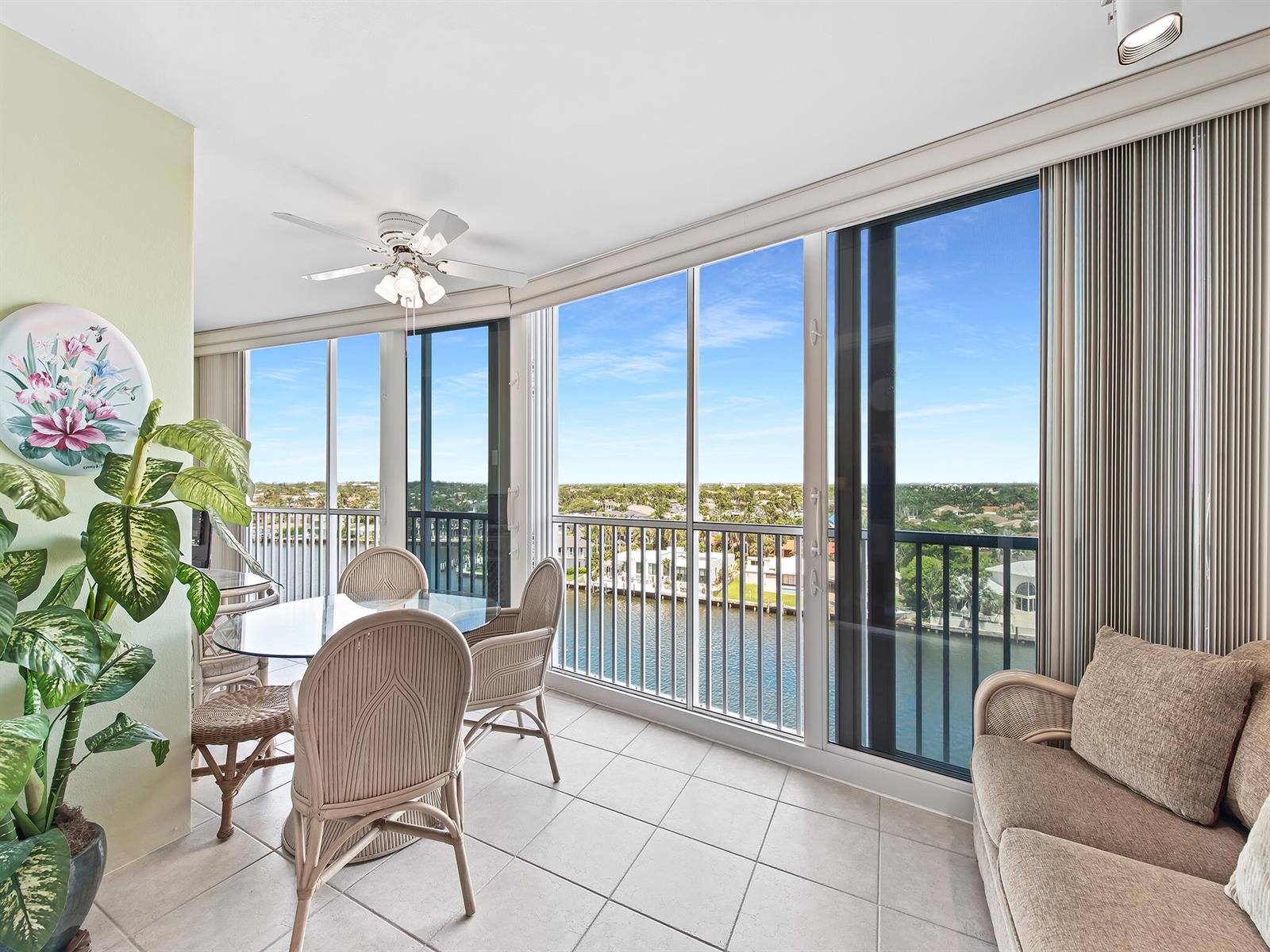 A sunroom with a dining set and sofa overlooks a canal through large glass windows — 3310 S Ocean Boulevard # 928d, Highland Beach FL 33487, HIGHLAND BEACH, FL