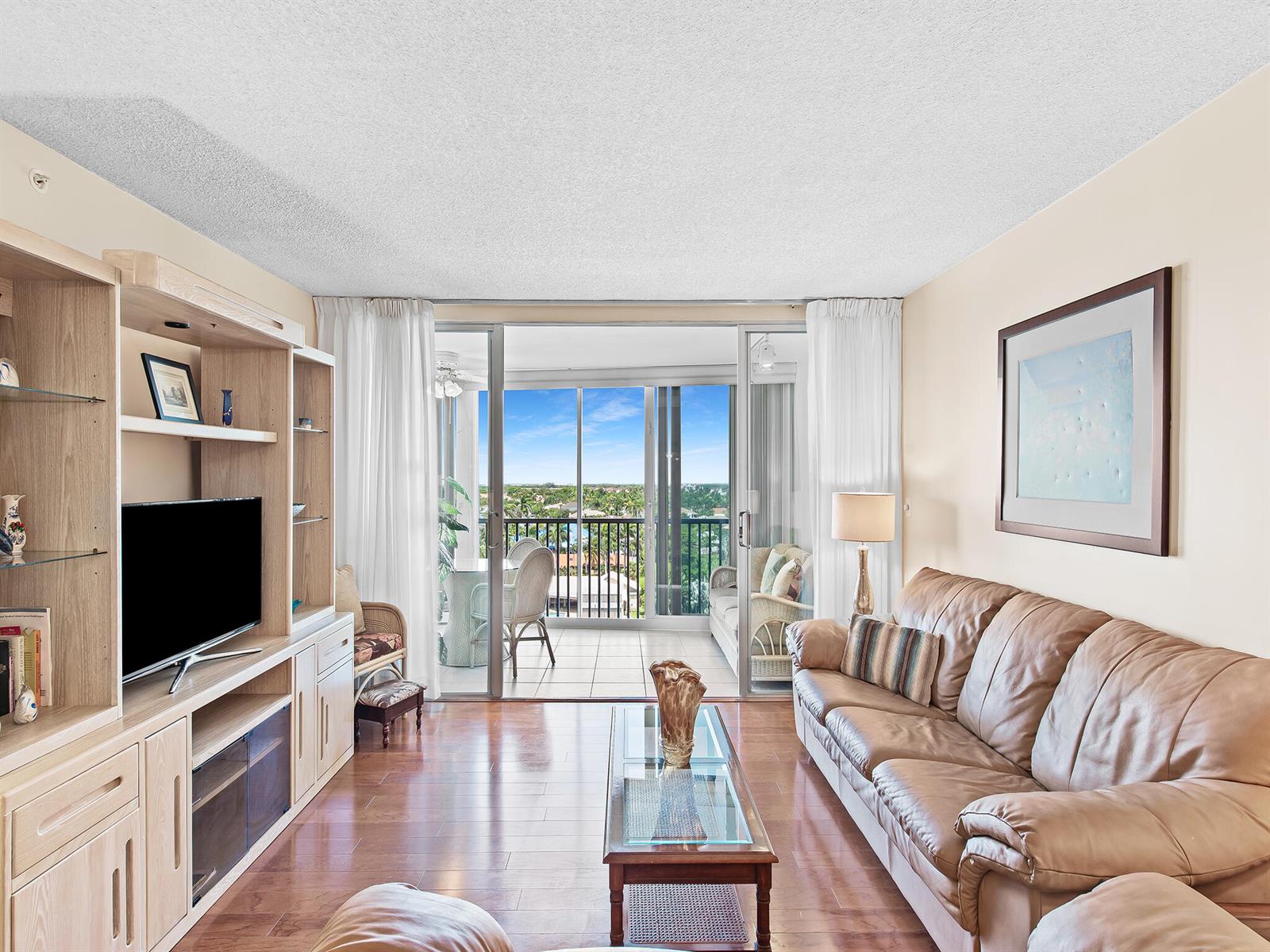 A living room features a leather sofa, wood flooring, and a balcony with a water view — 3310 S Ocean Boulevard # 928d, Highland Beach FL 33487, HIGHLAND BEACH, FL