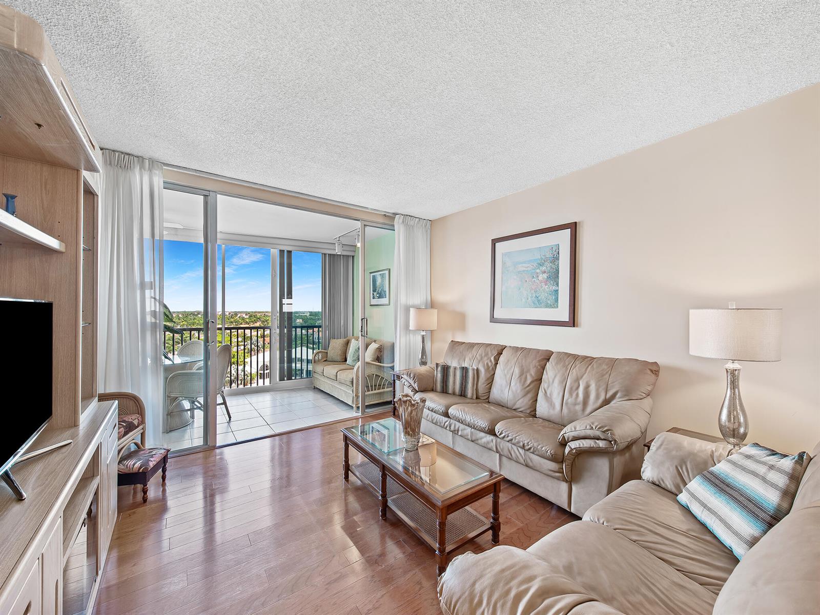 A living room with leather sofas, a glass coffee table, wood floors, and a balcony view — 3310 S Ocean Boulevard # 928d, Highland Beach FL 33487, HIGHLAND BEACH, FL