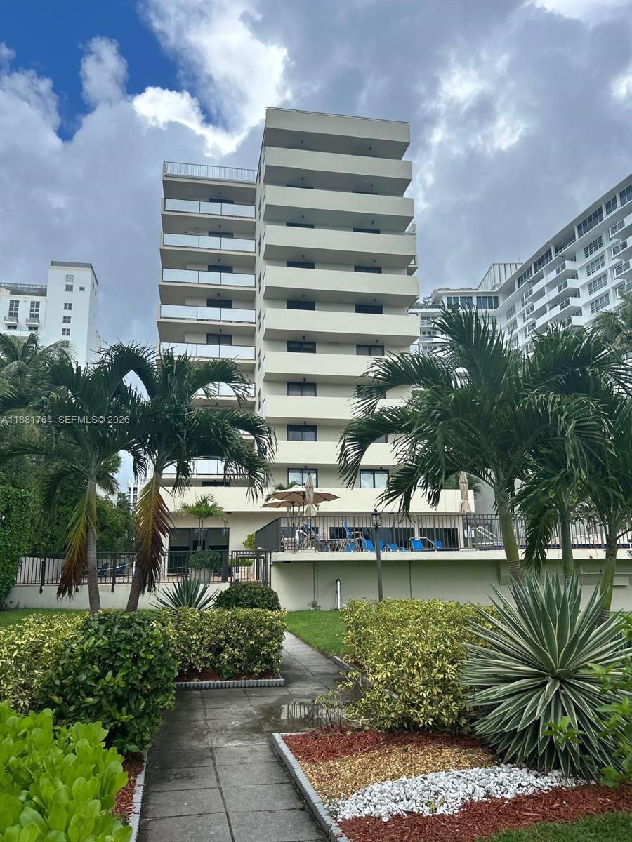 A multi-story residential building with balconies stands behind a landscaped garden and pool deck — 1621 Collins Ave # 701, Miami Beach FL 33139, MIAMI BEACH, FL