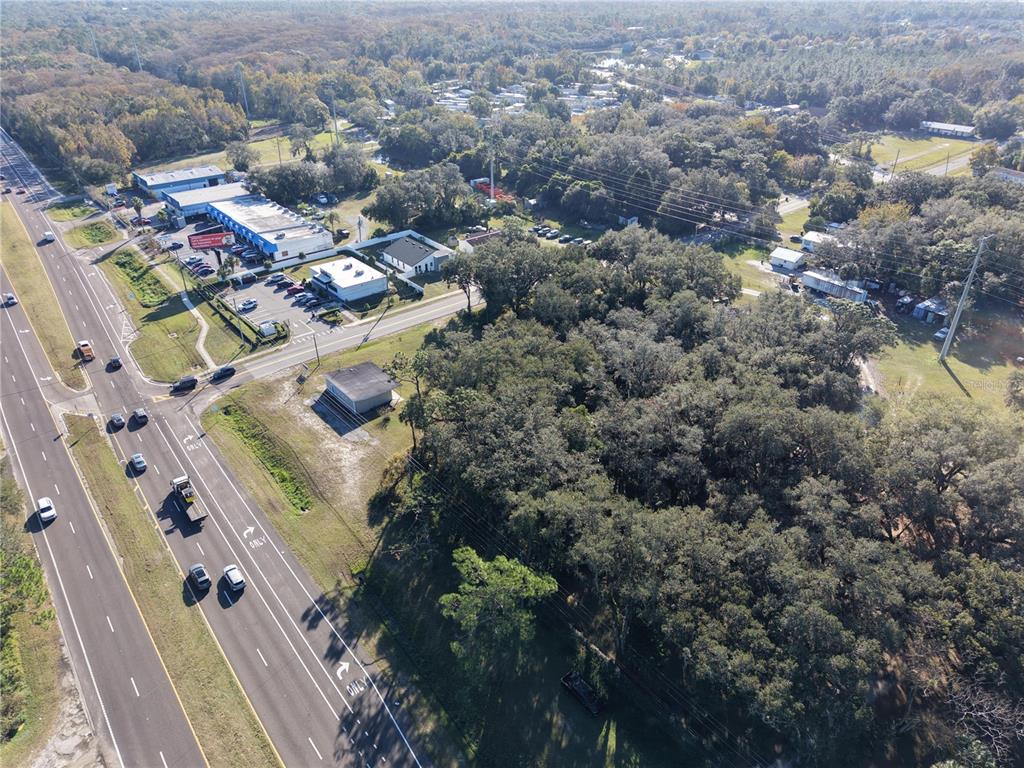 An aerial view shows a wooded lot adjacent to a multi-lane highway and commercial buildings — 15192 E COLONIAL DR, ORLANDO, FL
