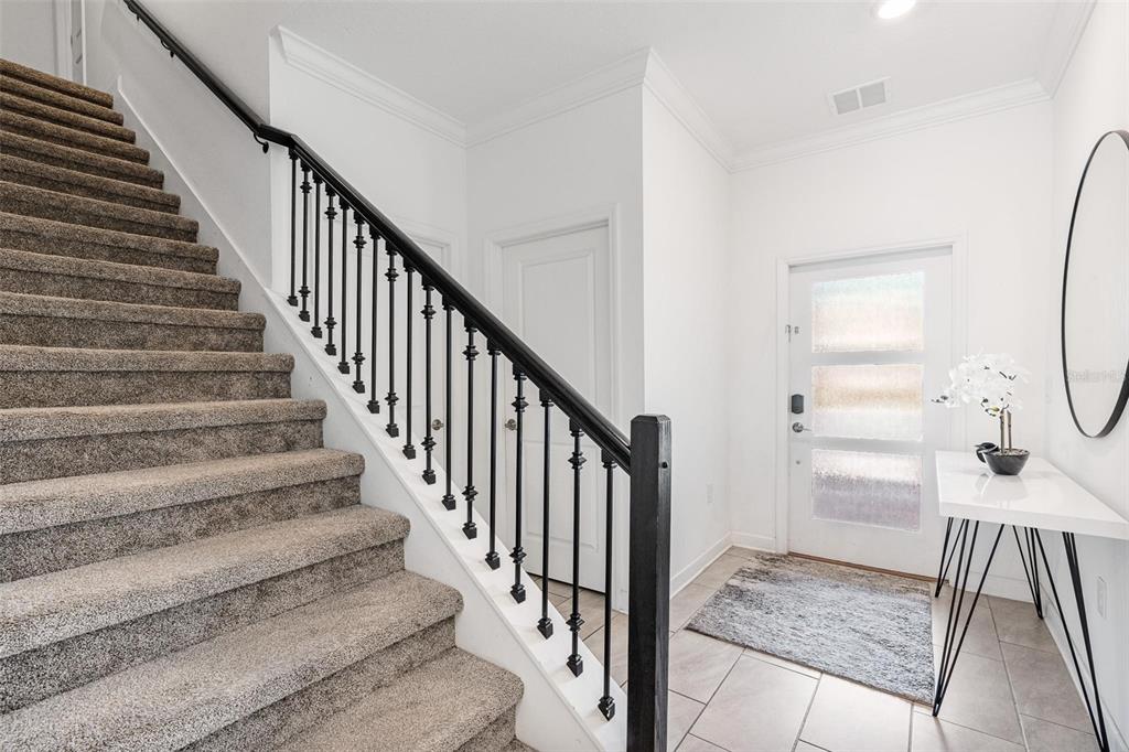 An entryway features a carpeted staircase with black railings, a white front door, and console table — 2957 PENELOPE LOOP, KISSIMMEE, FL