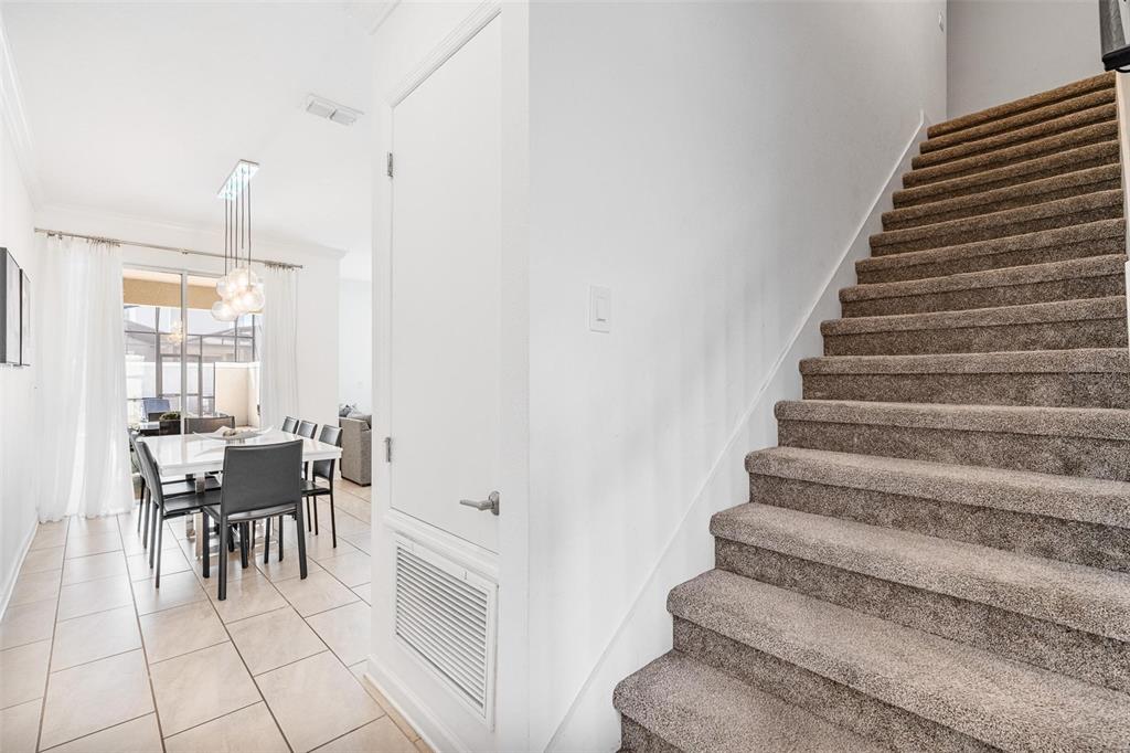 A carpeted staircase sits beside a dining area with a modern light fixture and tile — 2957 PENELOPE LOOP, KISSIMMEE, FL