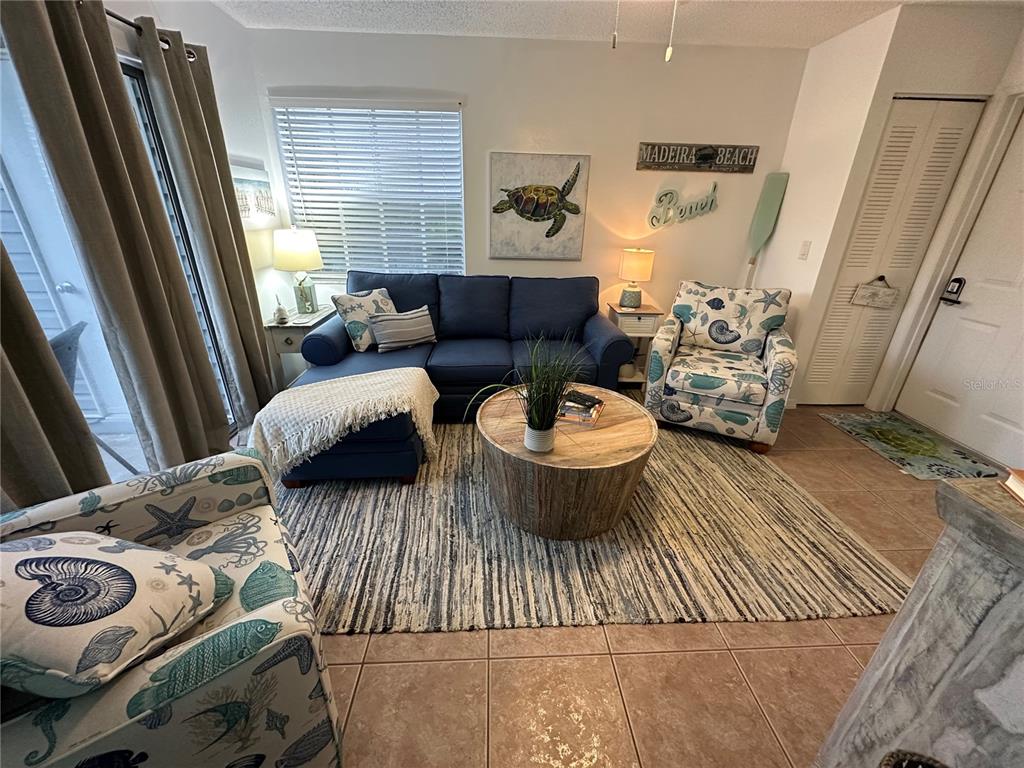 A living room features a blue sofa, two patterned armchairs, and a round wooden coffee table — 6825 STONES THROW CIRCLE N UNIT 1107, ST PETERSBURG, FL