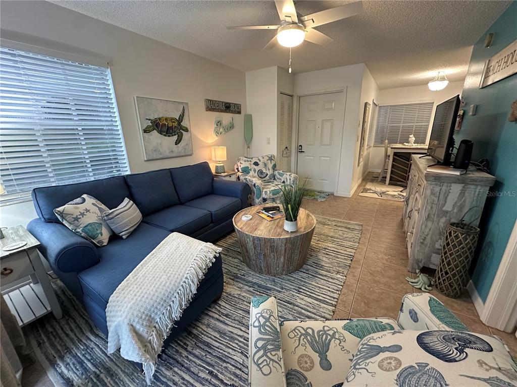 A living room features a blue sectional sofa, patterned armchairs, a round coffee table, and tile flooring — 6825 STONES THROW CIRCLE N UNIT 1107, ST PETERSBURG, FL